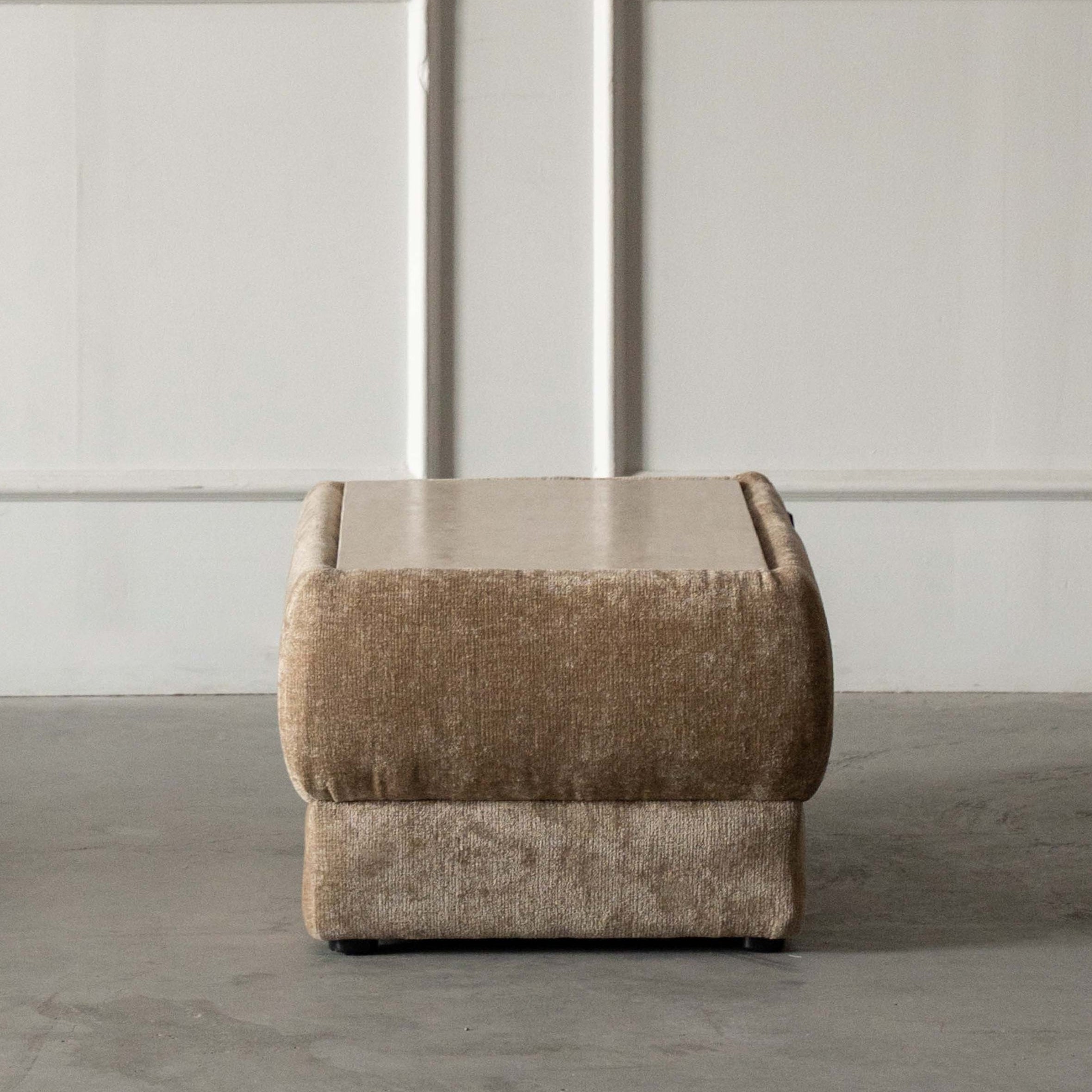 Beige ottoman on a concrete floor with a white paneled wall in the background