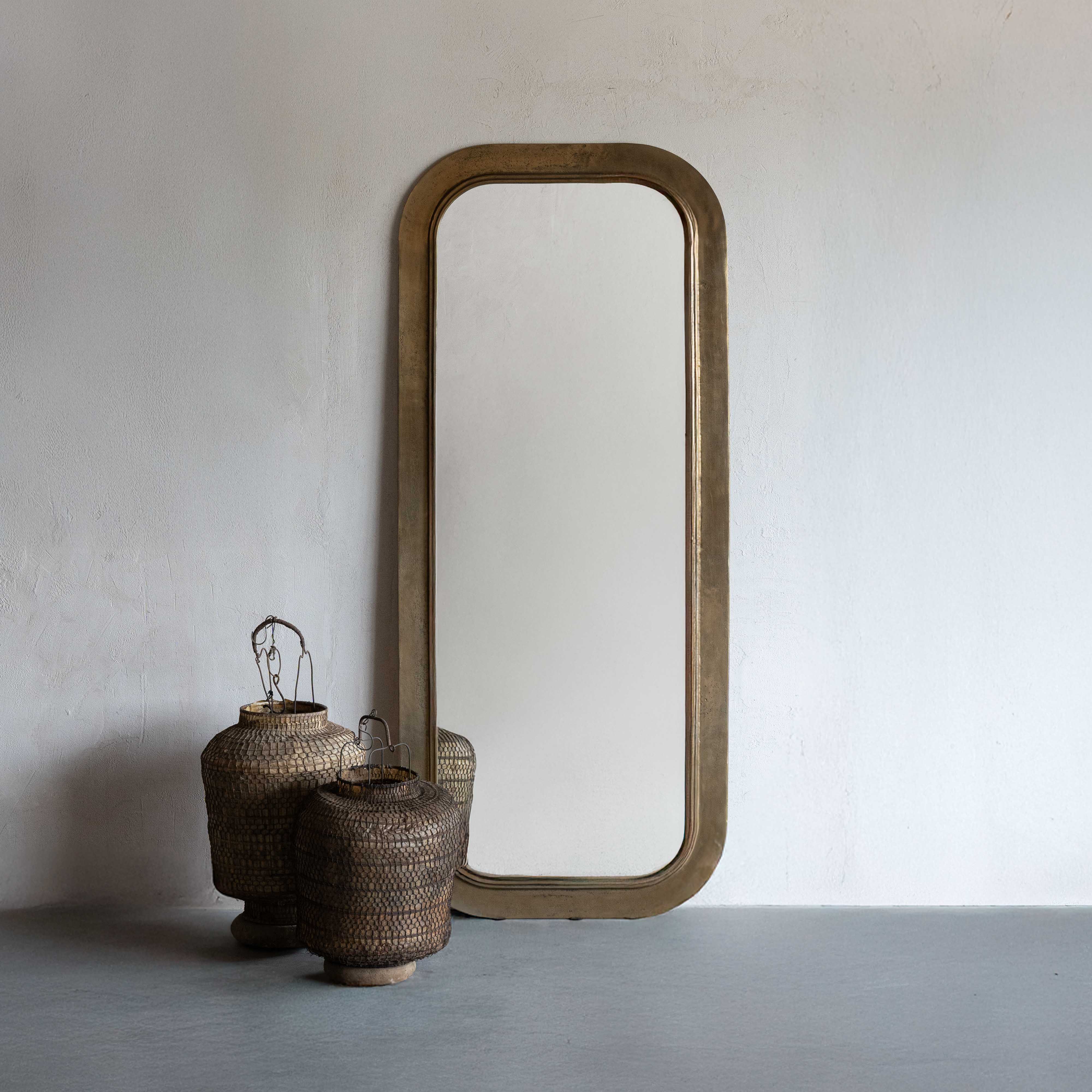 Wooden floor mirror with wicker baskets against a plain wall
