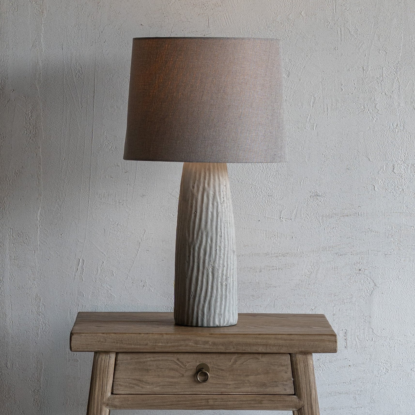 Table lamp with a textured base on a wooden side table against a plain wall.