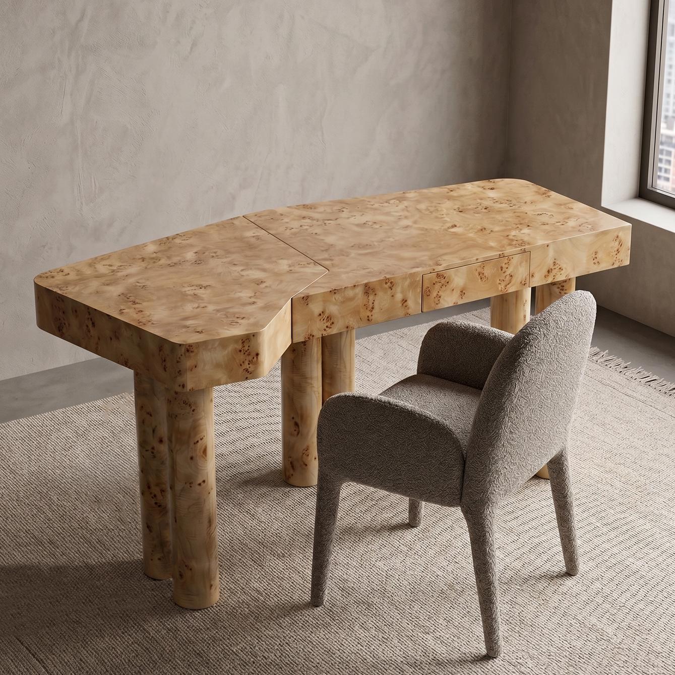 A modern burl wood writing desk with a matching upholstered gray chair, set on a textured rug against a neutral concrete wall.