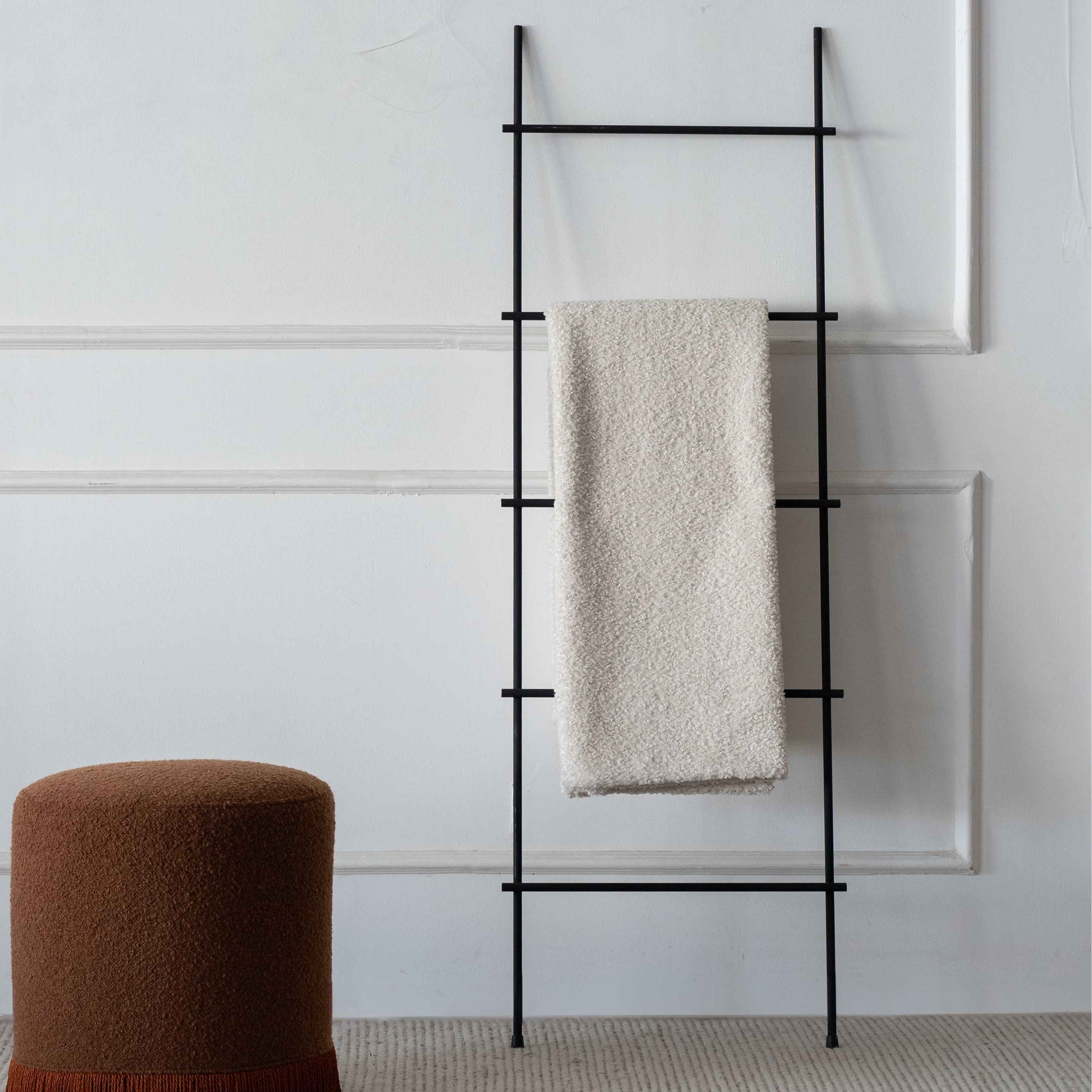 Black towel rack with a beige towel against a white wall, brown stool on the left.