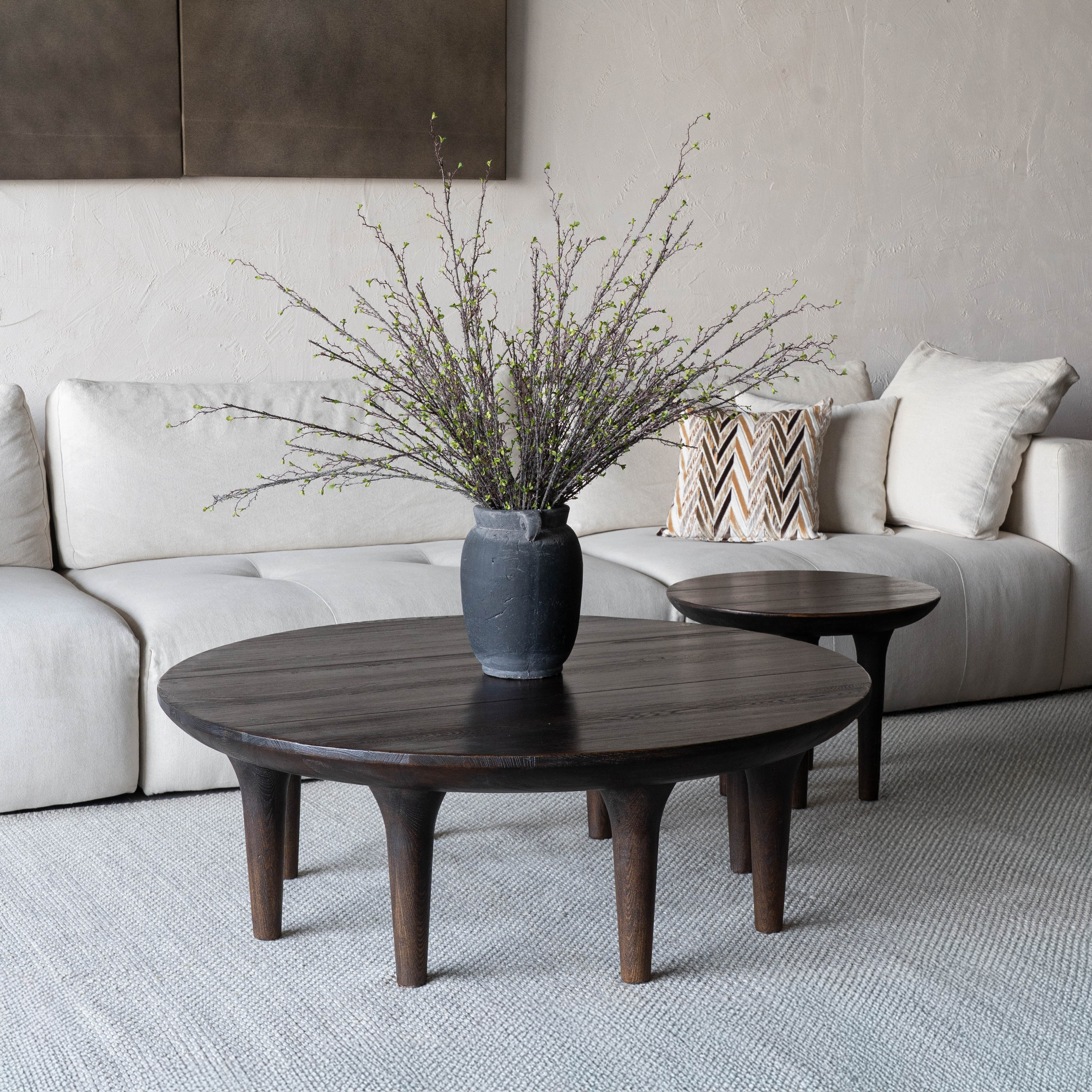 Living room with a beige sofa, wooden coffee table, and decorative vase with branches.