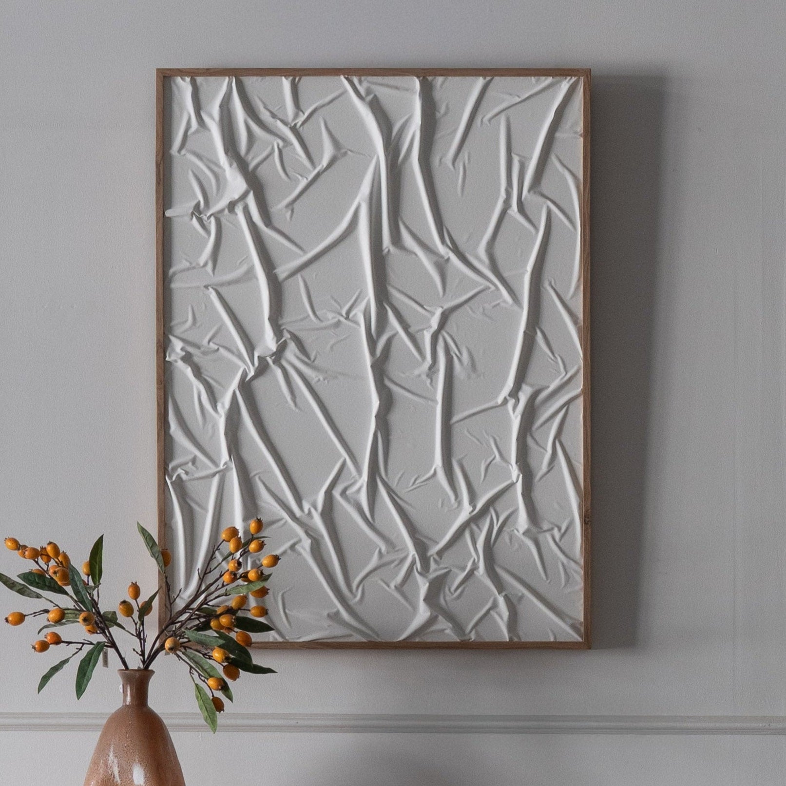 Abstract wall art with a vase and decorative items on a table against a gray wall.