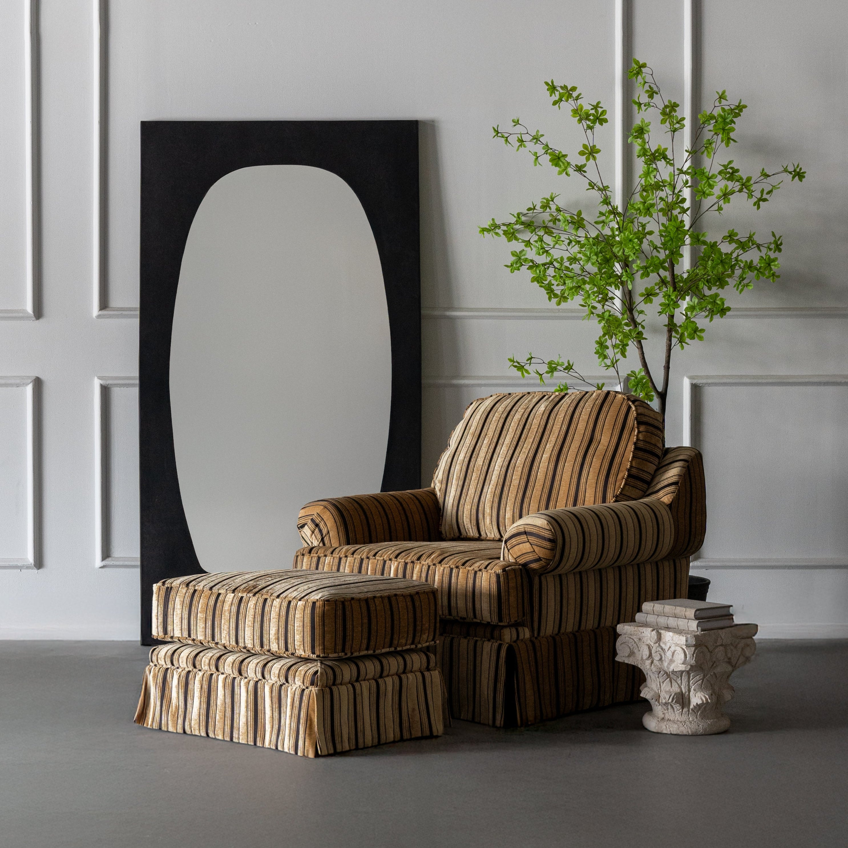 Striped armchair and ottoman with a mirror and plant in a room with white paneled walls.