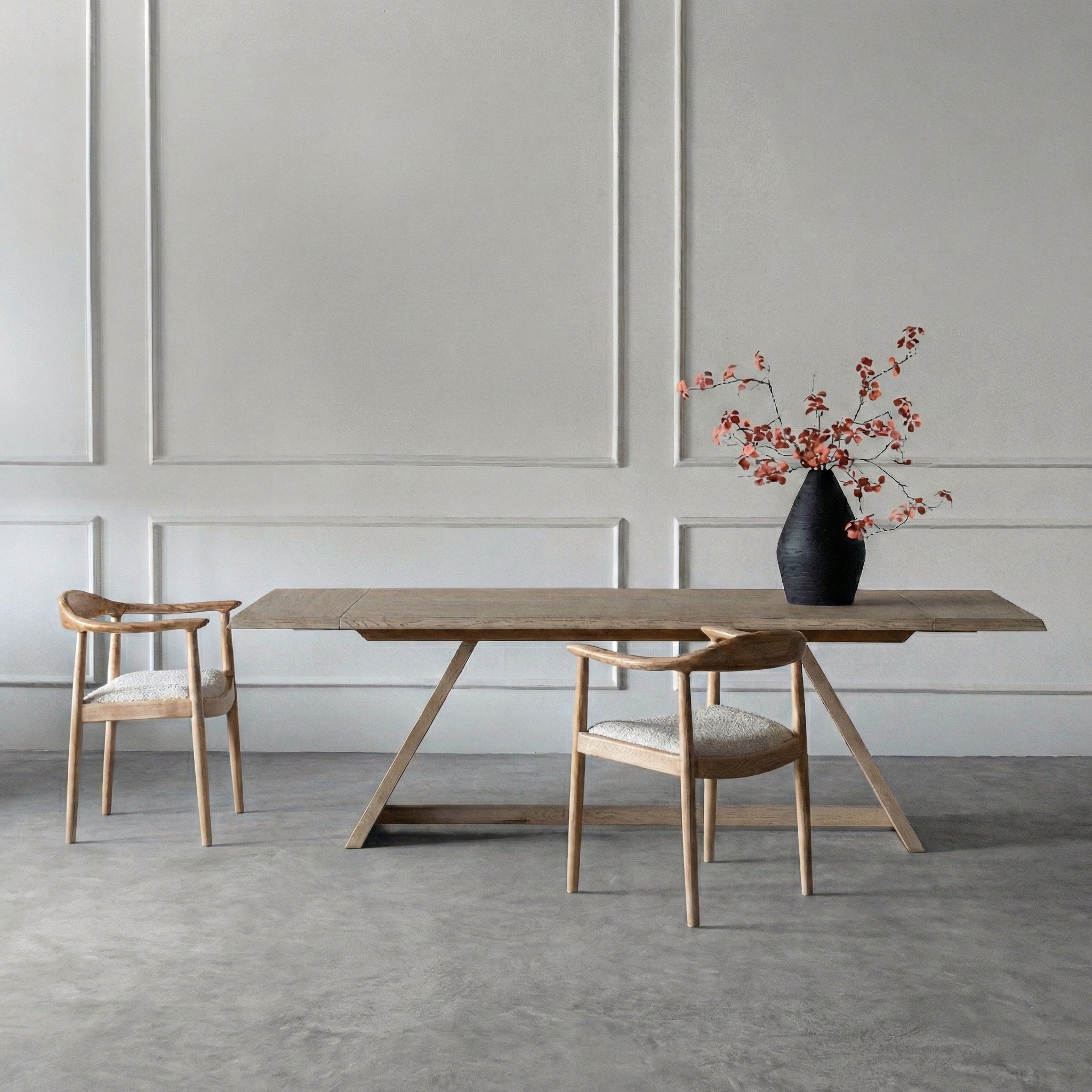 Dining table with two chairs and a vase of flowers against a neutral wall.