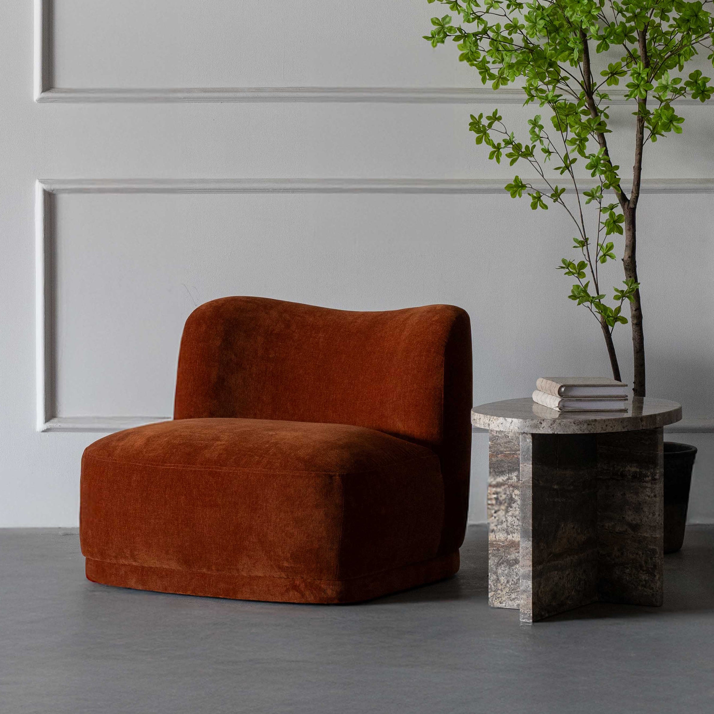 Brown armchair in a room with a gray wall and a small table with a plant.