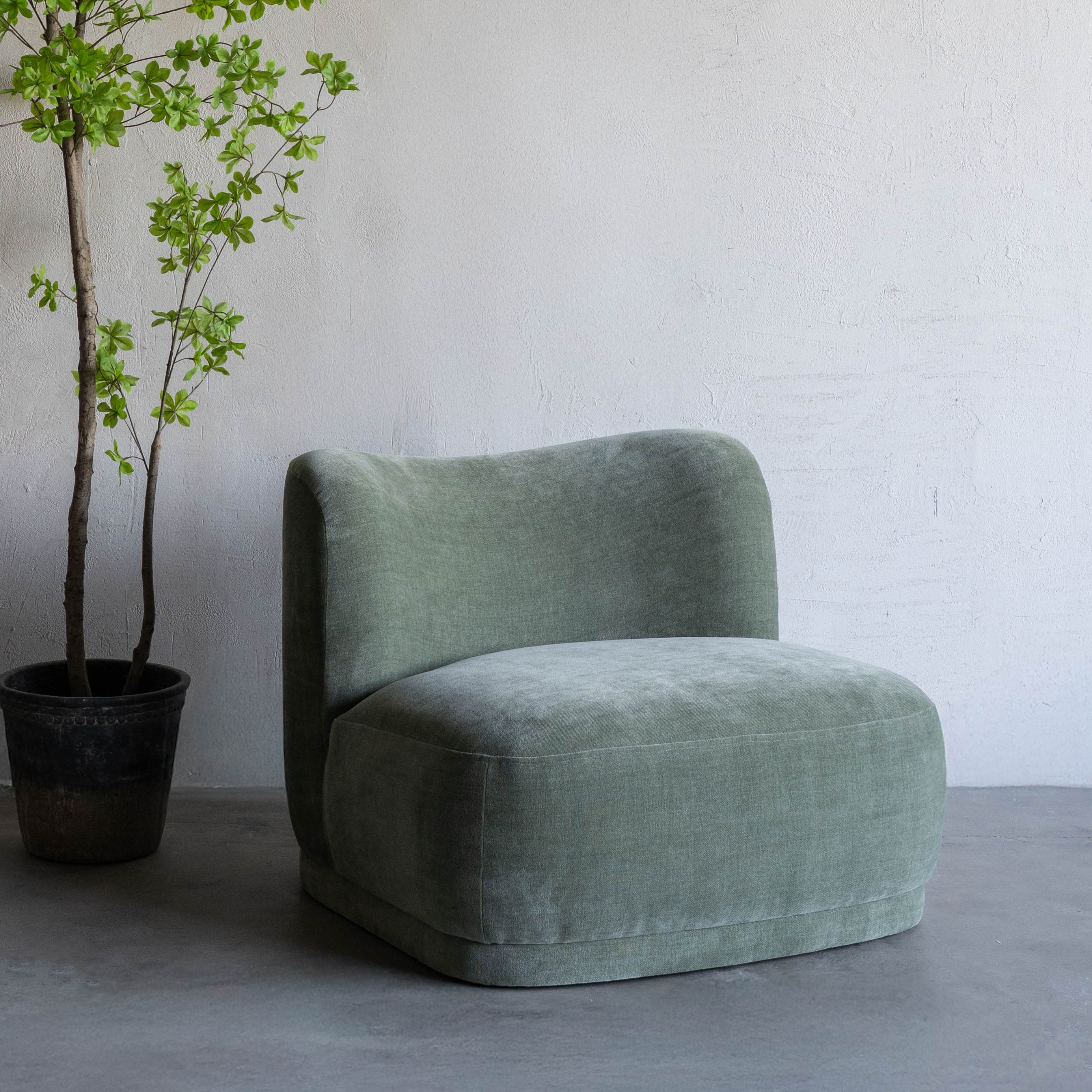 Green armchair next to a potted plant on a gray floor with a white wall background