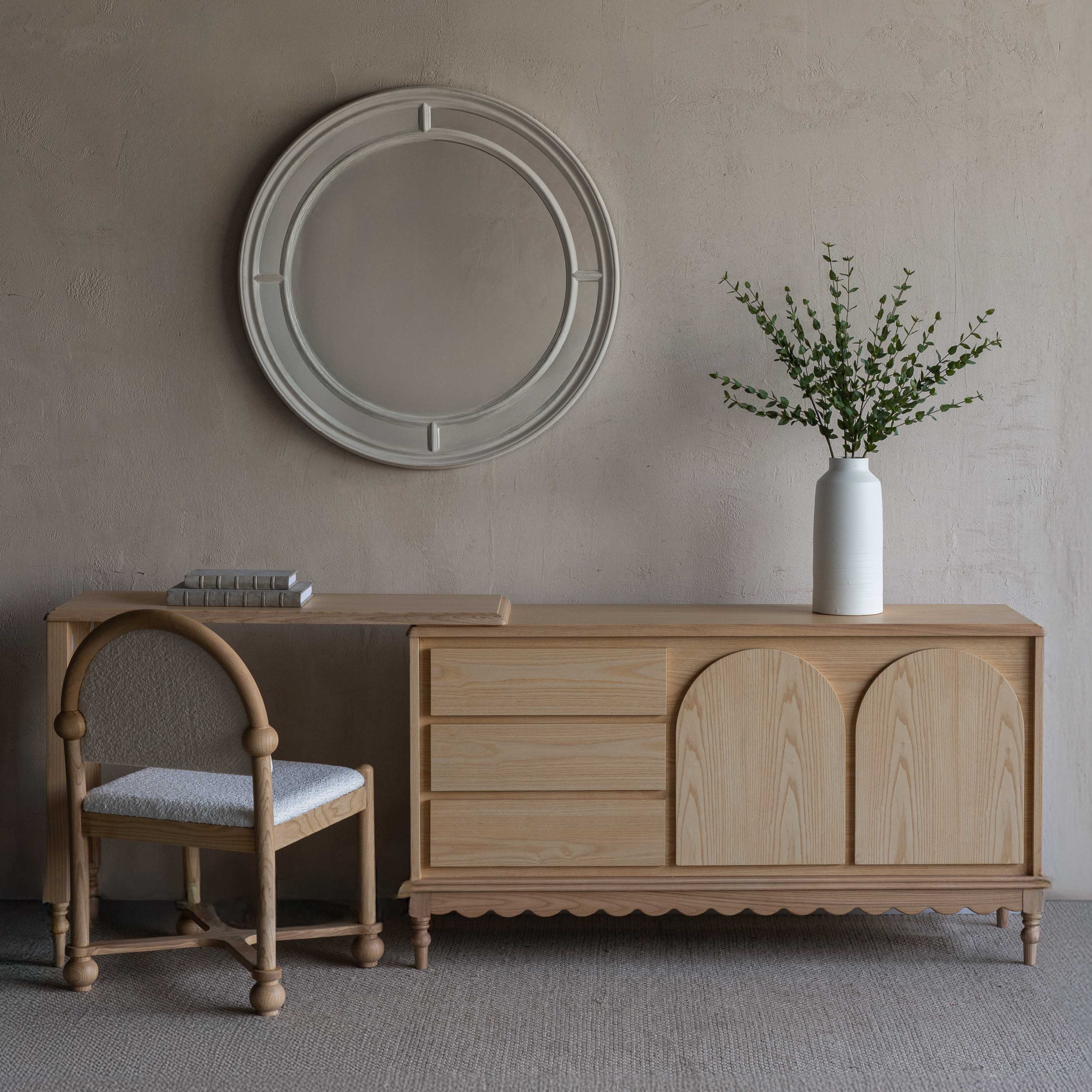 Wooden dresser with a chair and decorative items against a plain wall.