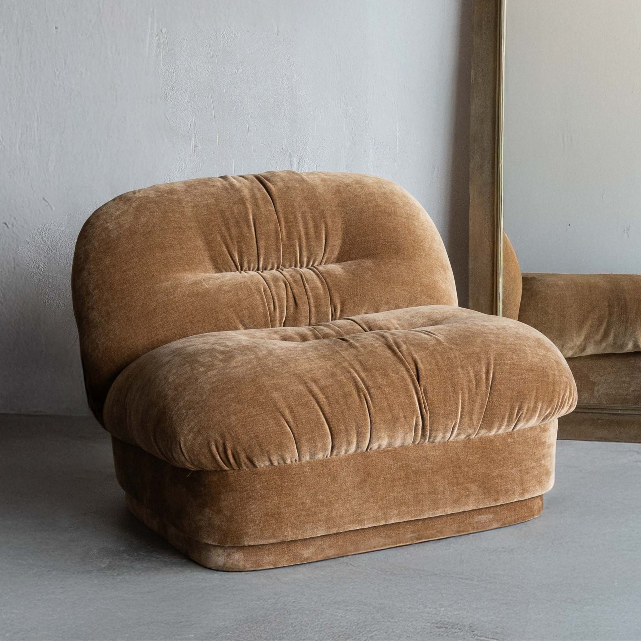 Brown velvet armchair and tall mirror against a plain wall.