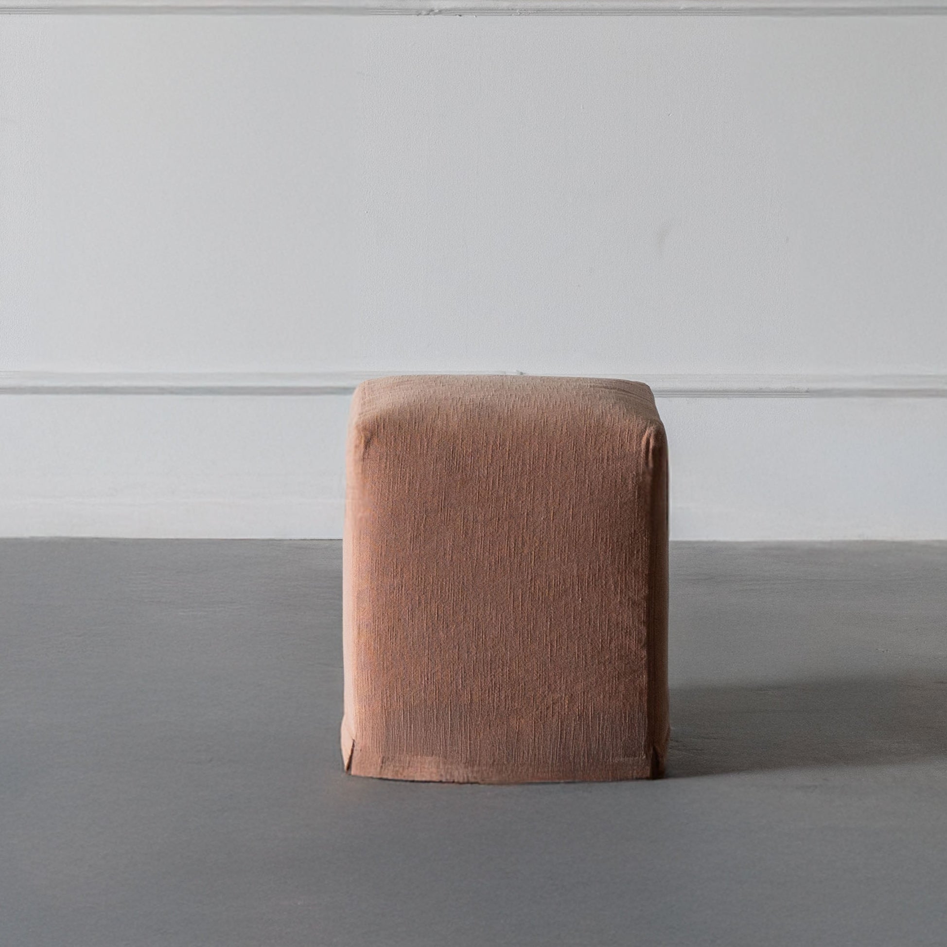 Brown cube-shaped ottoman against a white paneled wall.