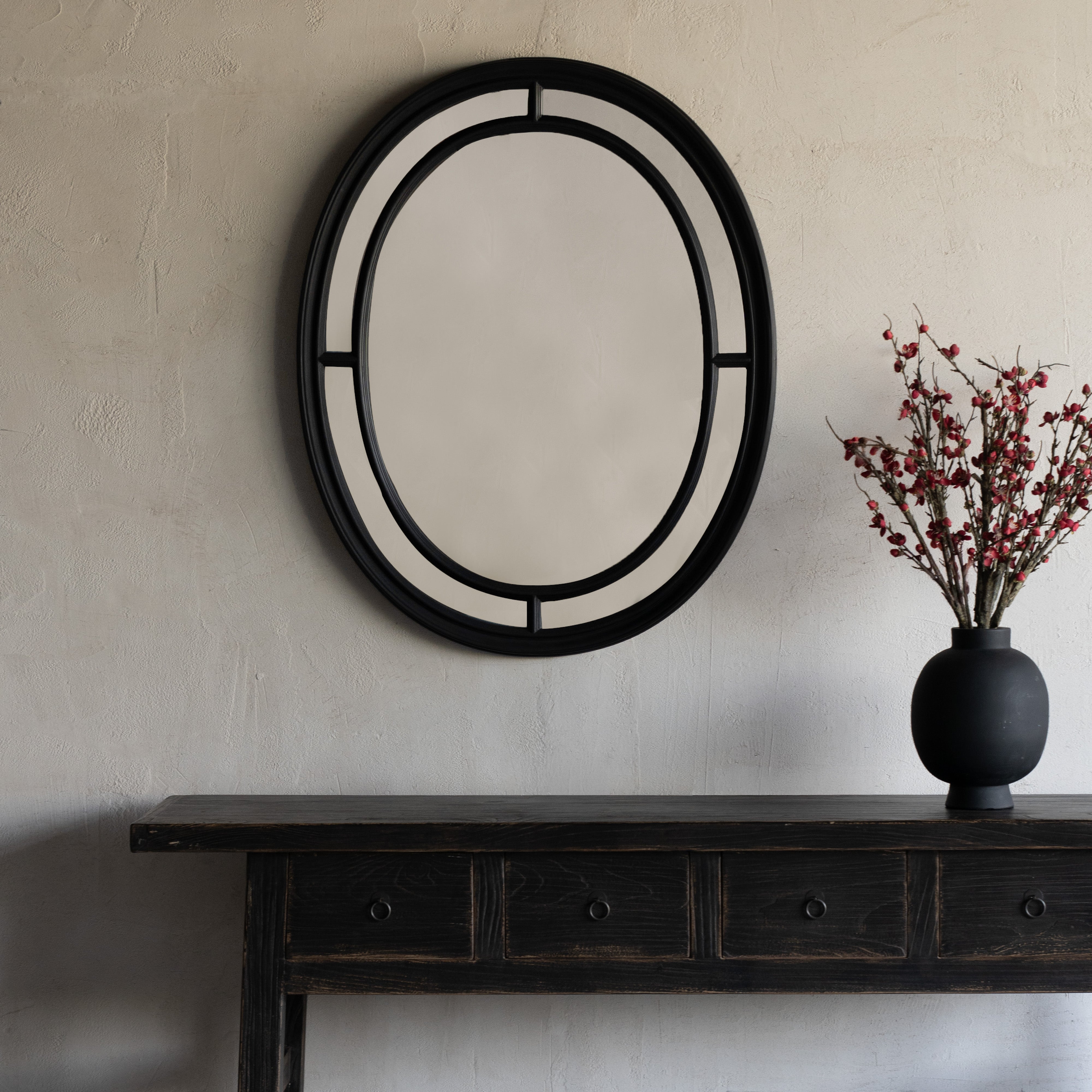 Decorative mirror with black frame on a plain wall above a dark wooden console table.