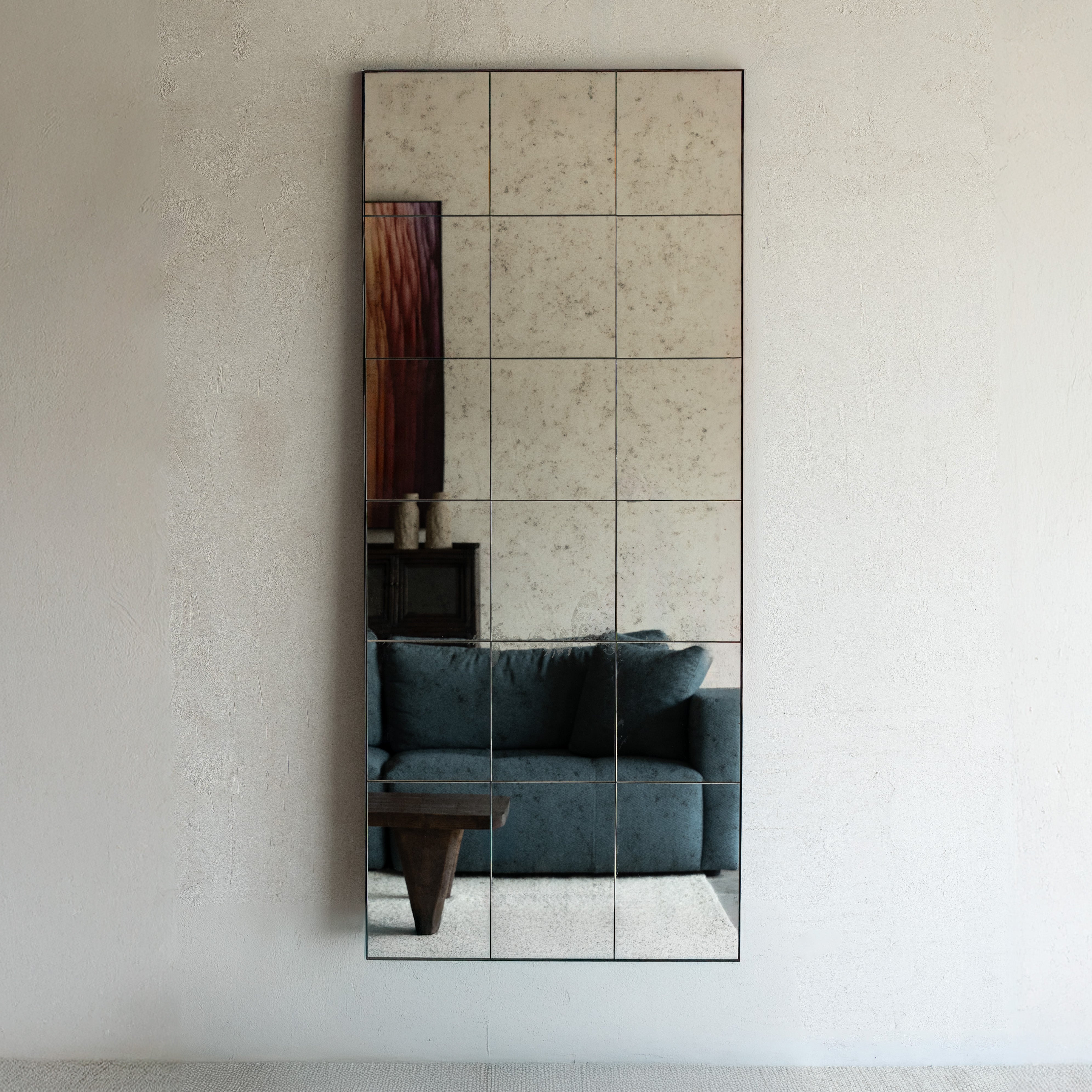 Wall-mounted mirror with a geometric design reflecting a room with a blue sofa.