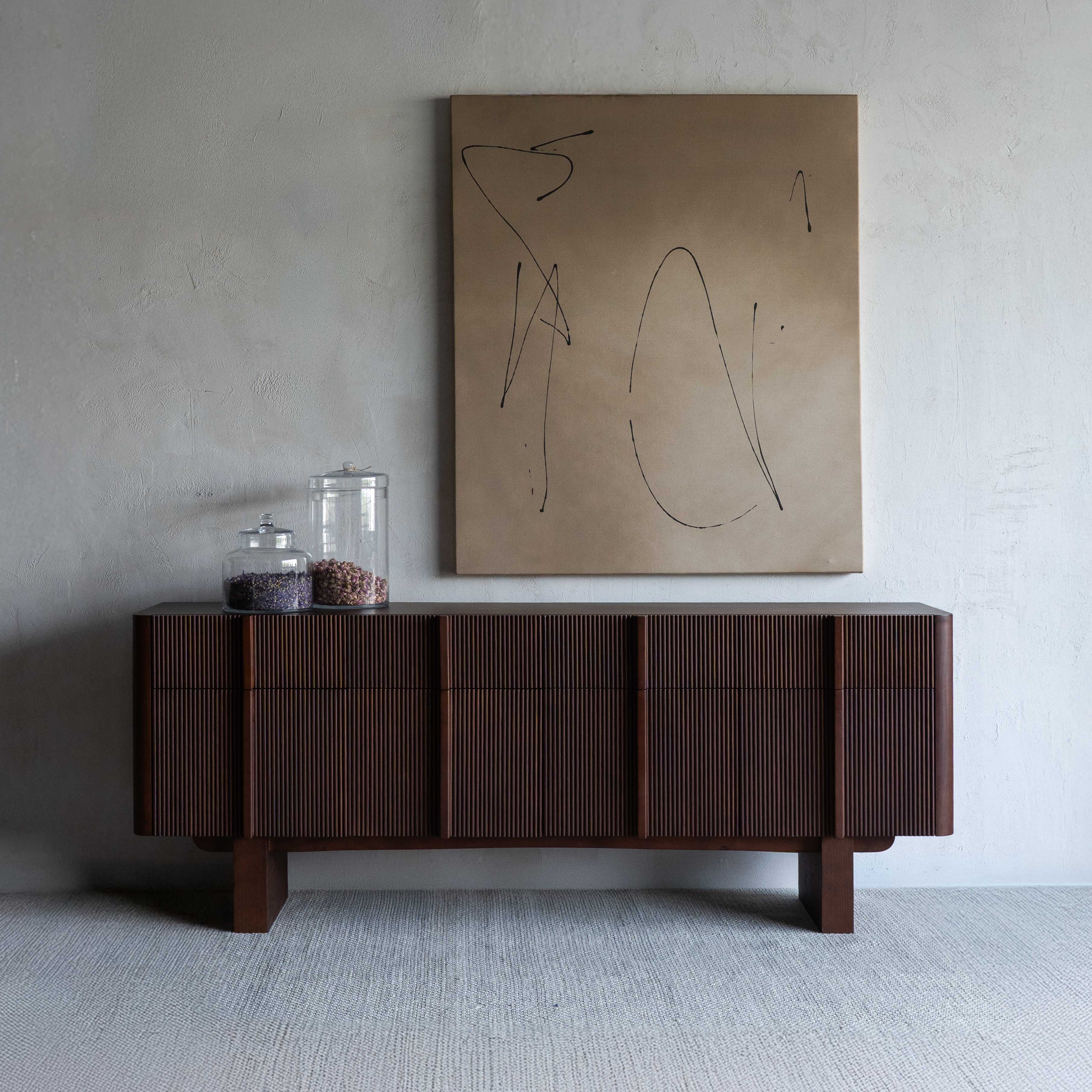 Wooden sideboard with decorative items against a plain wall with abstract art.