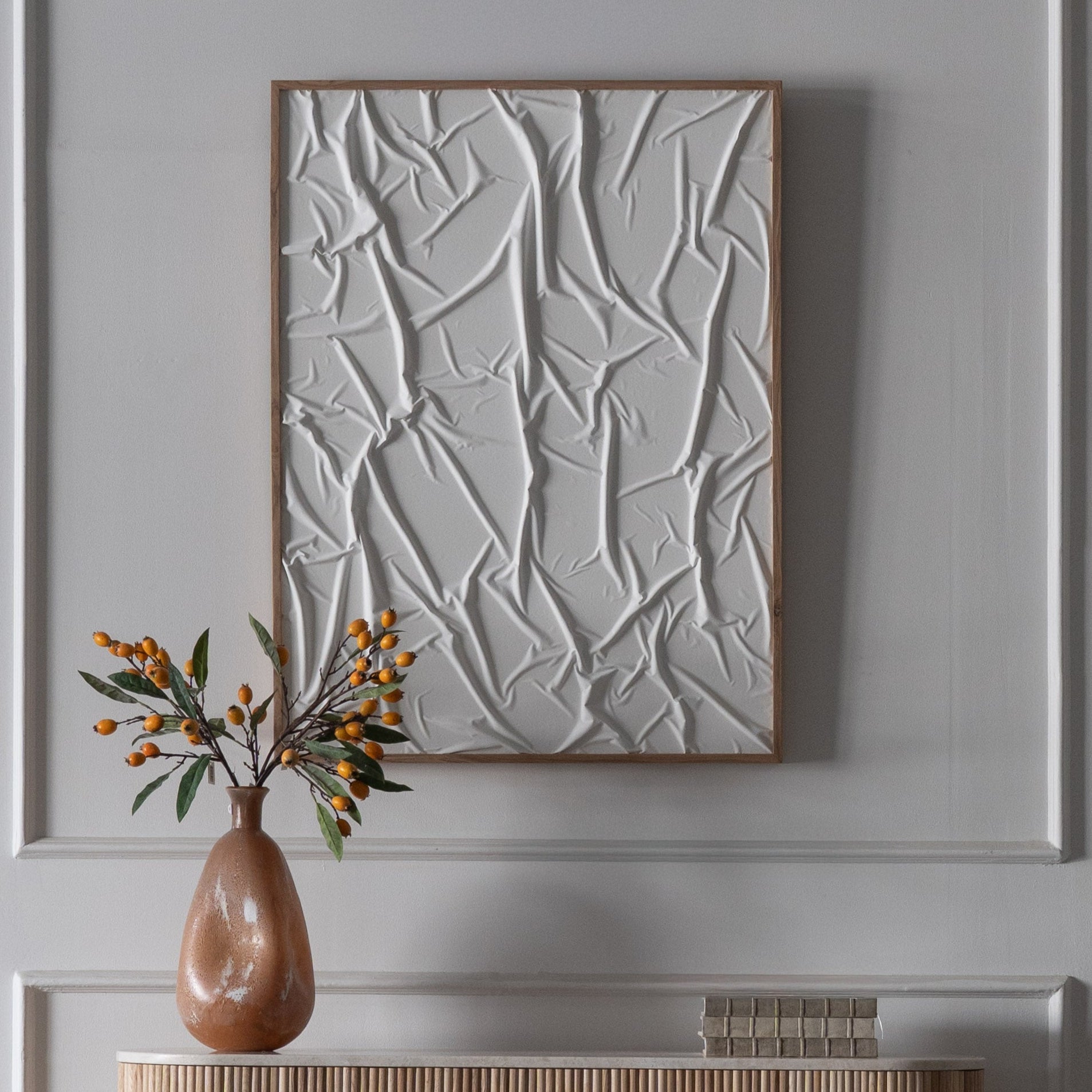 Abstract wall art with a vase and decorative items on a table against a gray wall.