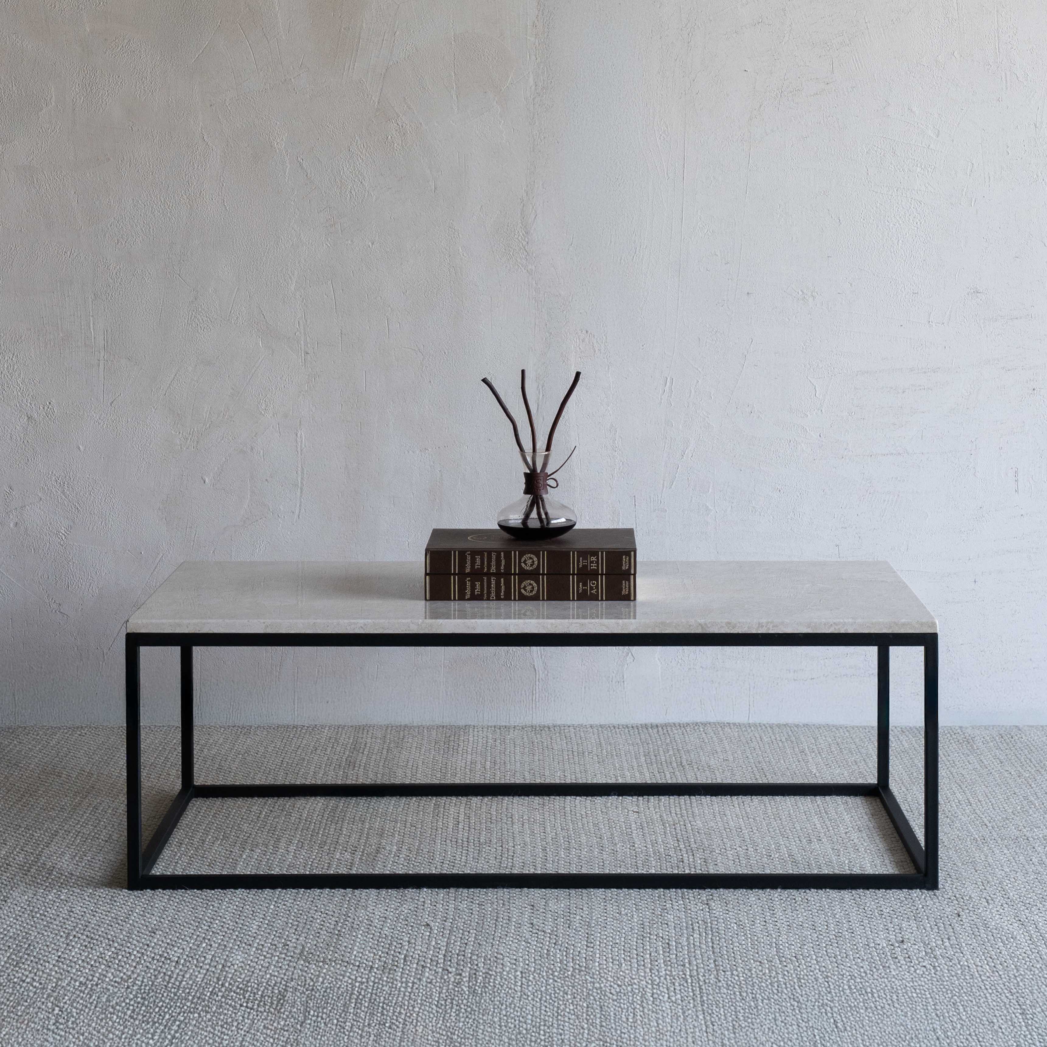 Coffee table with a black frame and white marble top, featuring a book and decorative items against a plain wall.