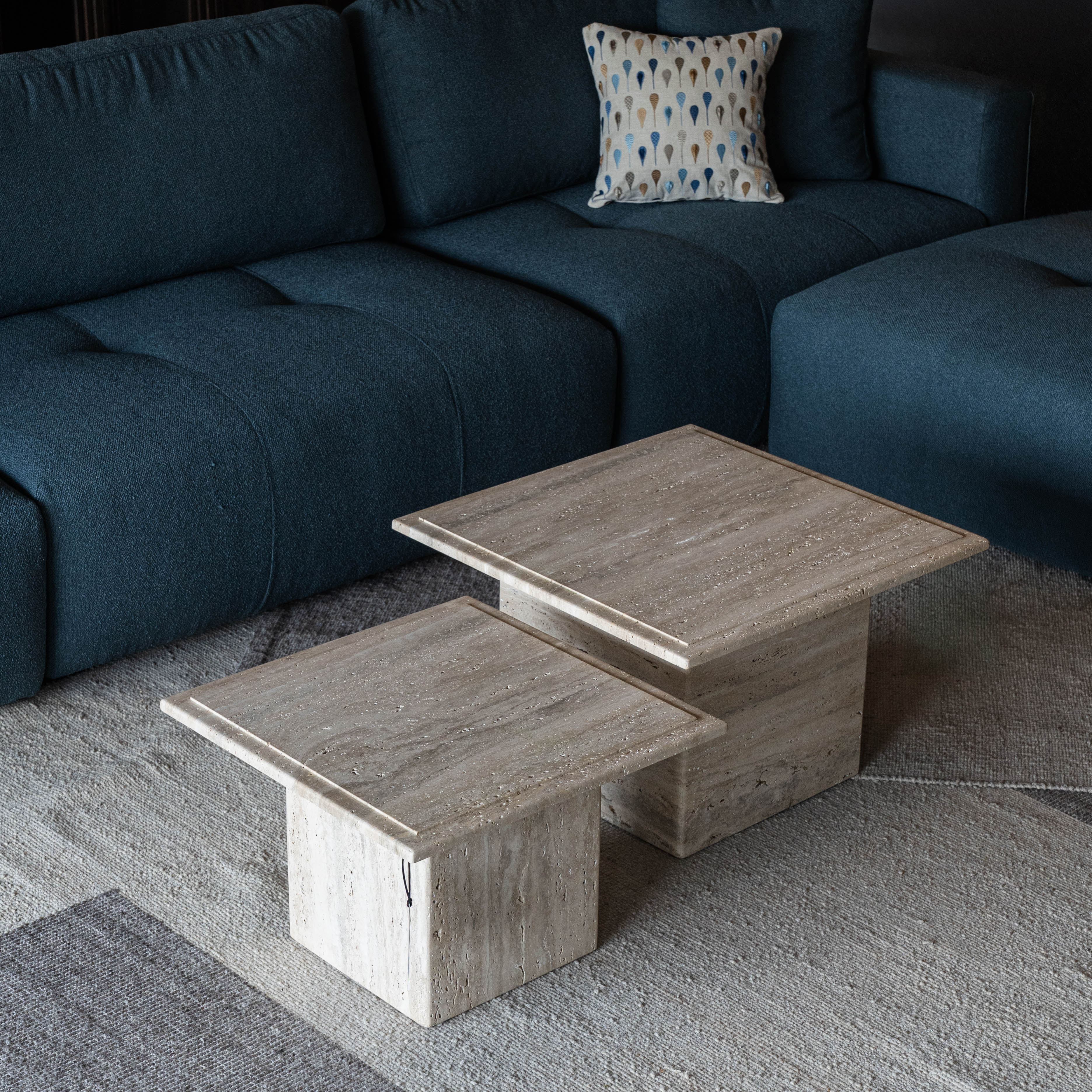 travertine coffee table with a dark blue sofa and patterned pillow in a living room setting.