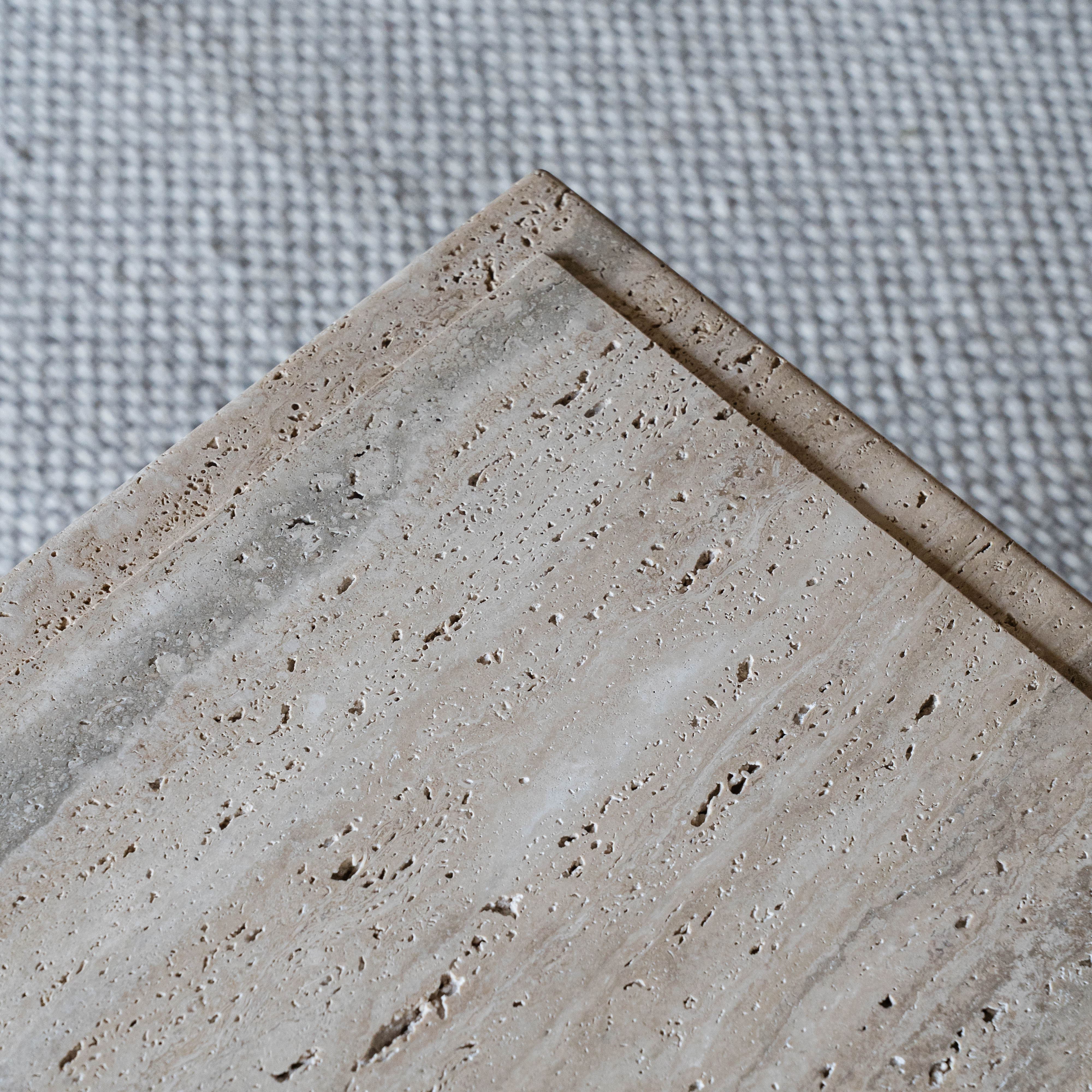 Close-up of a beige stone tile with a textured surface on a gray fabric background