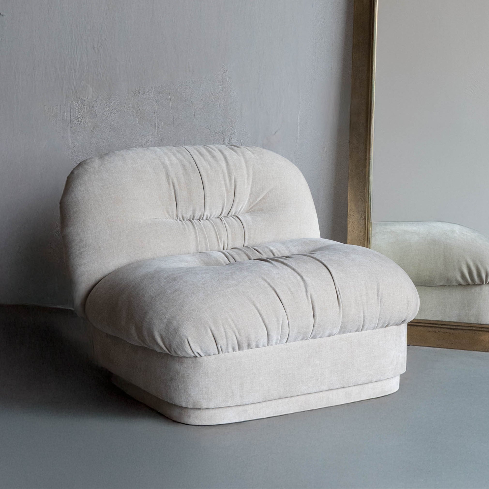 Beige armchair and tall mirror with wooden frame against a plain wall.