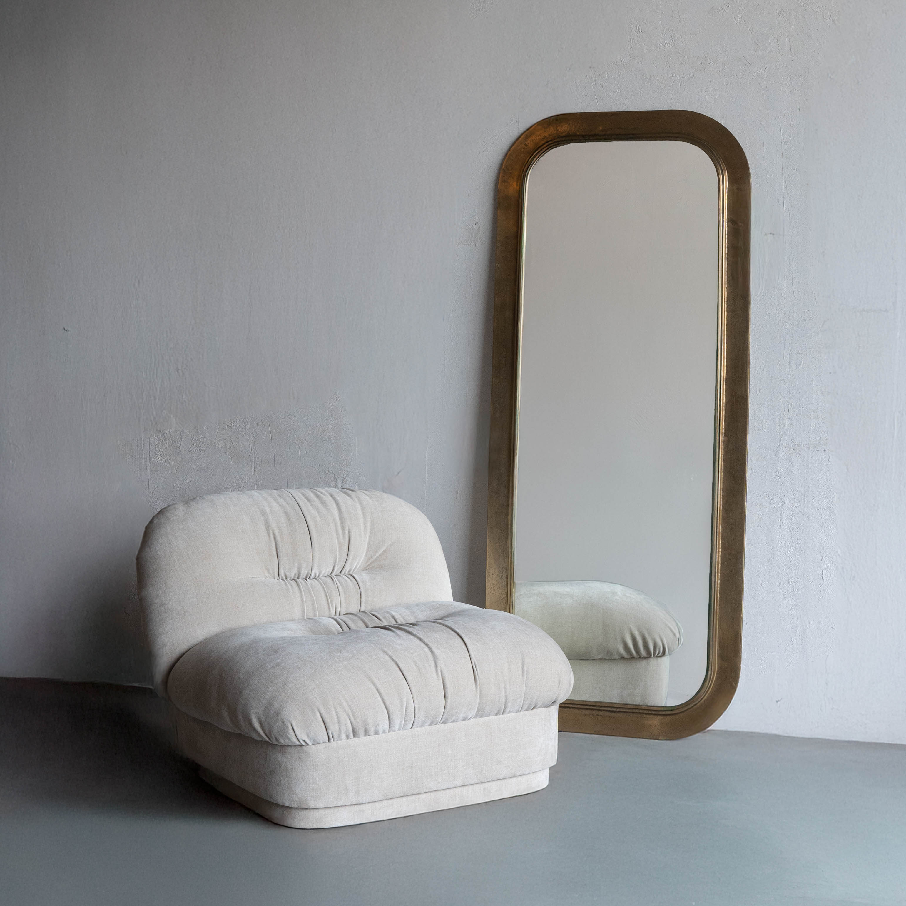 Beige armchair and tall mirror with wooden frame against a plain wall.