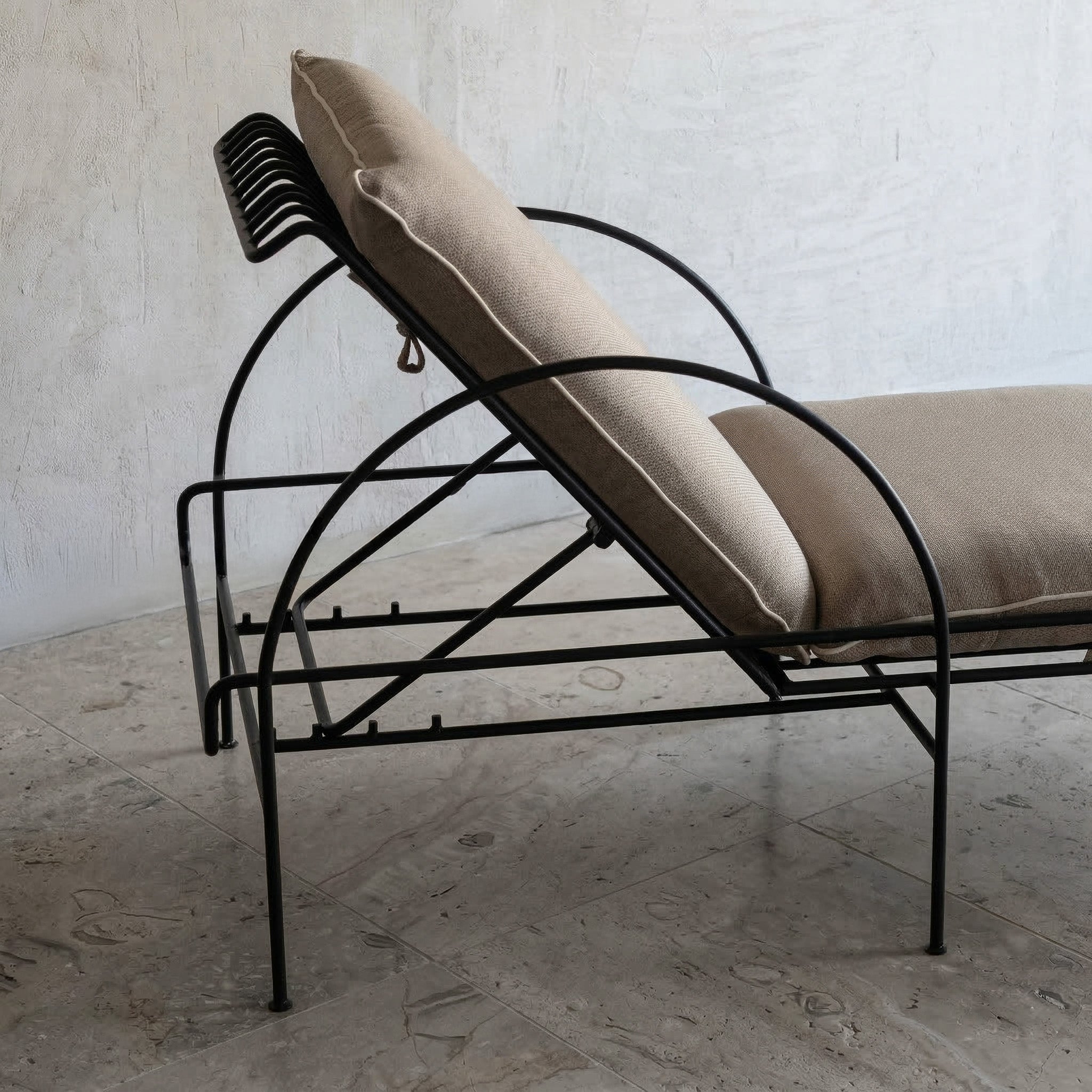 Wrought iron chaise lounge with beige cushions against a textured wall.