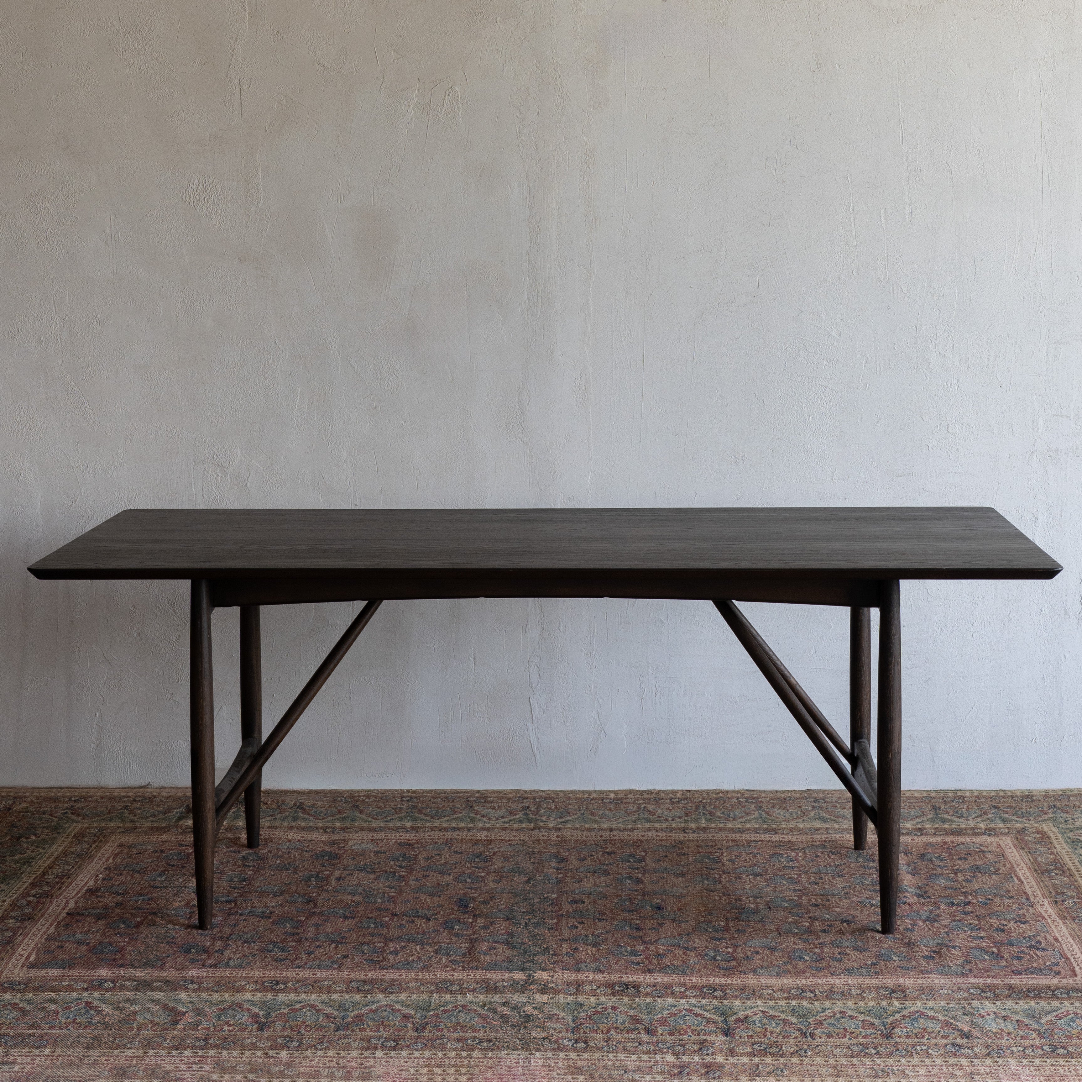 Dark wooden dining table against a plain wall with a textured rug below.