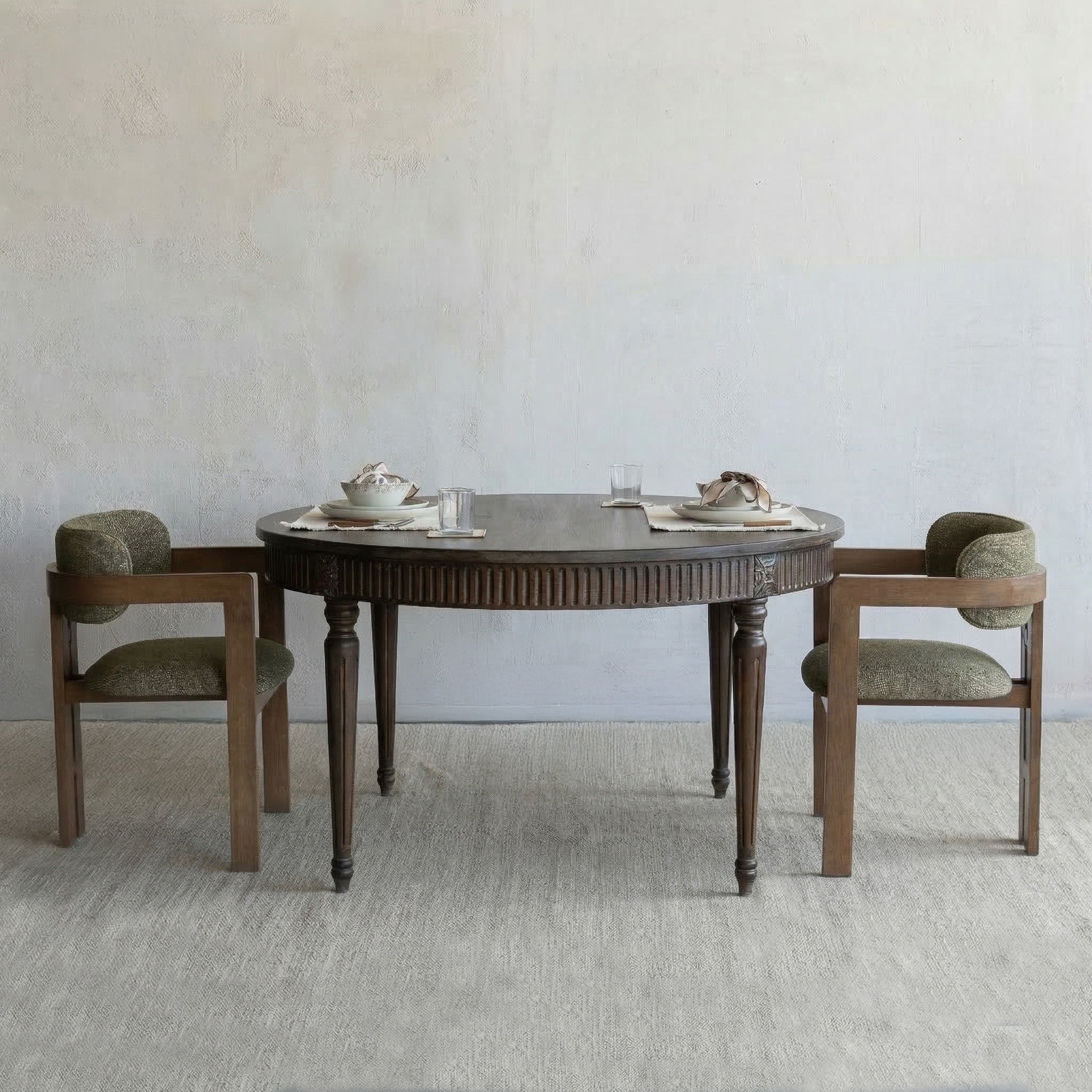Round wooden dining table with two chairs against a plain wall.