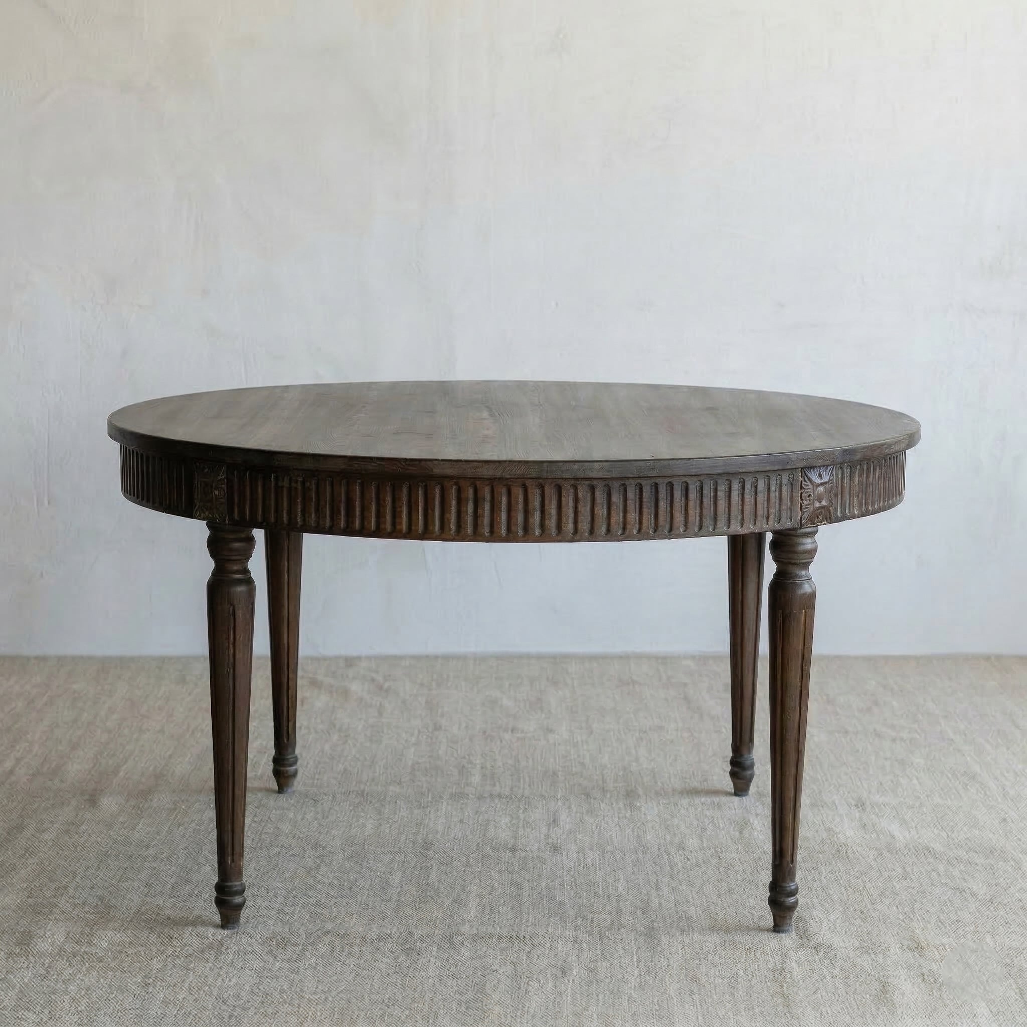 Round wooden table with a ribbed surface on a plain floor and wall background